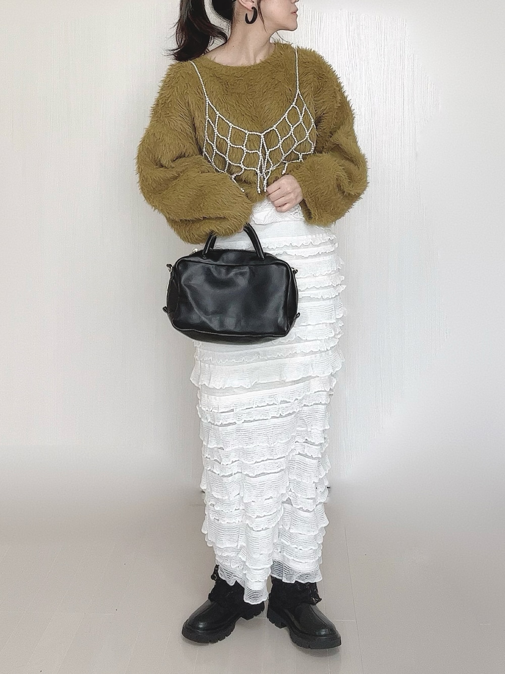 グリーン系のニット/セーター、ホワイト系のベスト、ブラック系のボストンバッグを着用したレディースの冬コーディネートの1枚目の写真