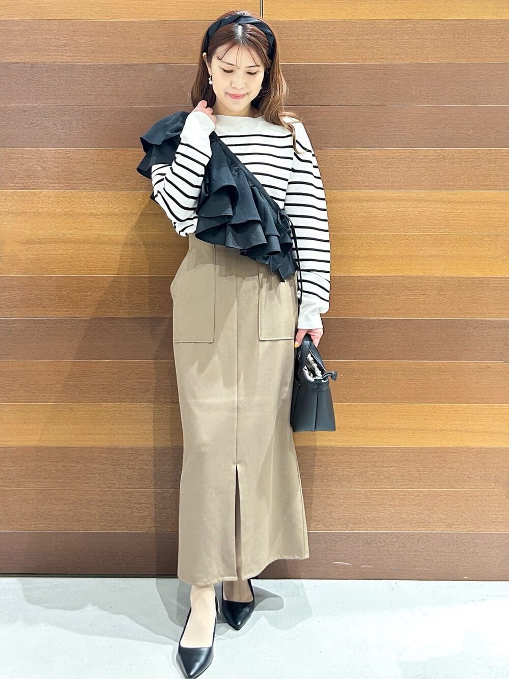 ブラック系のパンプス、ベージュ系のショルダーバッグ、ブラウン系のスカートを着用したレディースの春コーディネートの1枚目の写真