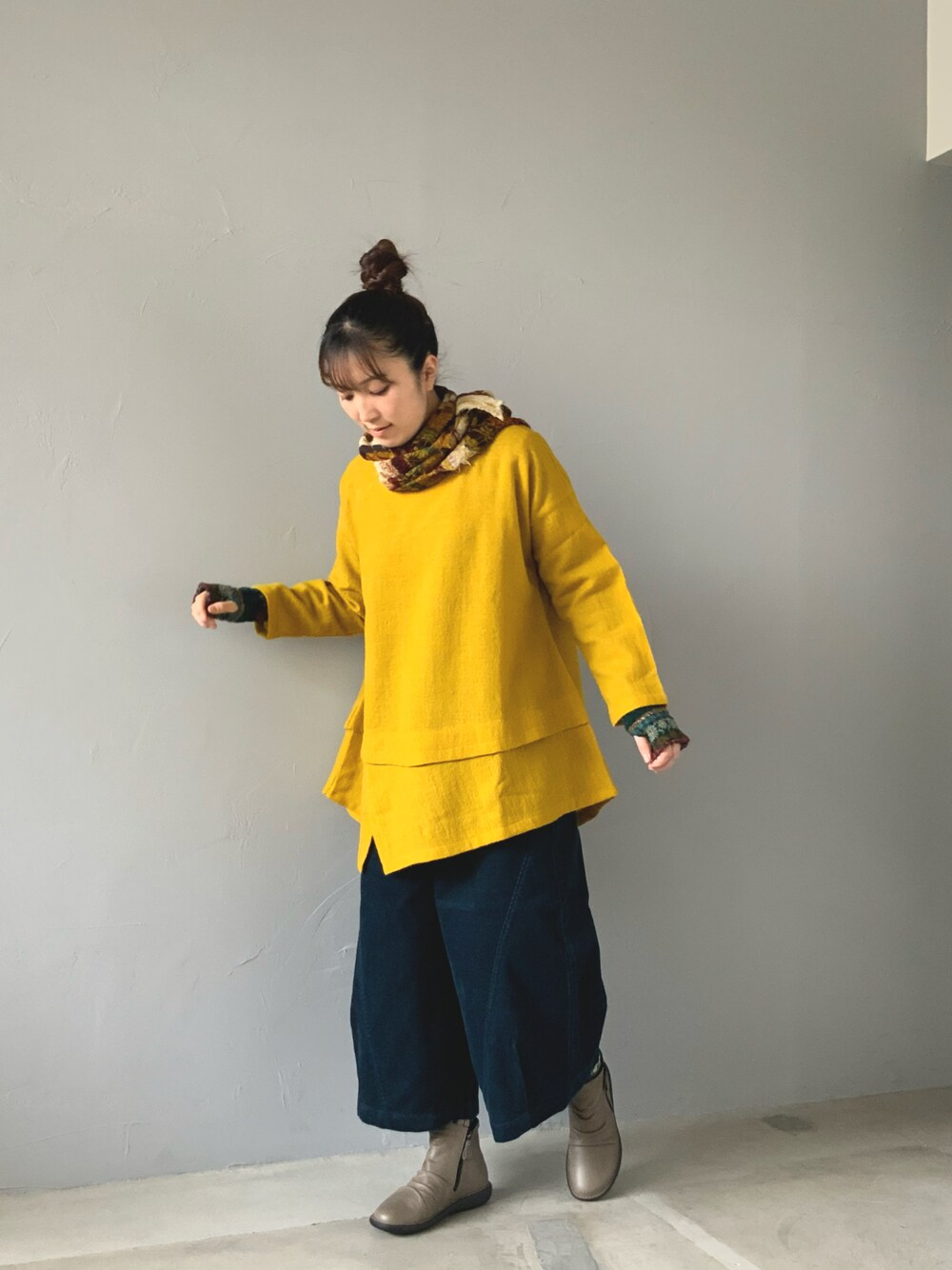 イエロー系のトップス、グリーン系のパンツ、グレー系のブーツを着用したレディースの秋コーディネートの1枚目の写真