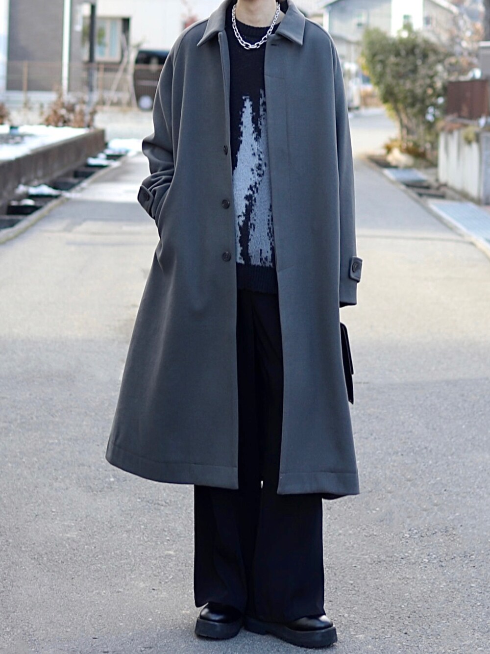 グレー系のステンカラーコート、ブラック系のニット/セーター、ブラック系のスラックスを着用したメンズの冬コーディネートの1枚目の写真