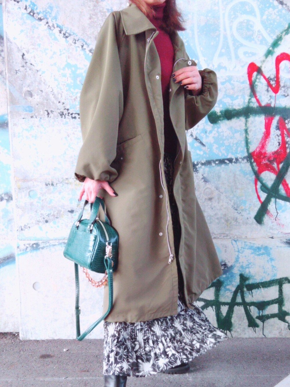 レッド系のニット/セーター、グリーン系のトレンチコート、ブラック系のスカートを着用したレディースの冬コーディネートの3枚目の写真