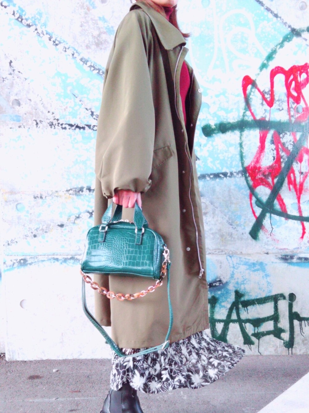 レッド系のニット/セーター、グリーン系のトレンチコート、ブラック系のスカートを着用したレディースの冬コーディネートの2枚目の写真