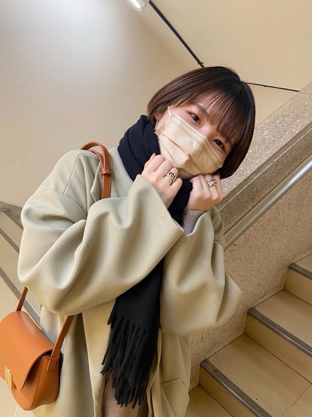 グリーン系のチェスターコート、ブラック系のショルダーバッグ、ベージュ系のワンピースを着用したレディースの冬コーディネートの1枚目の写真