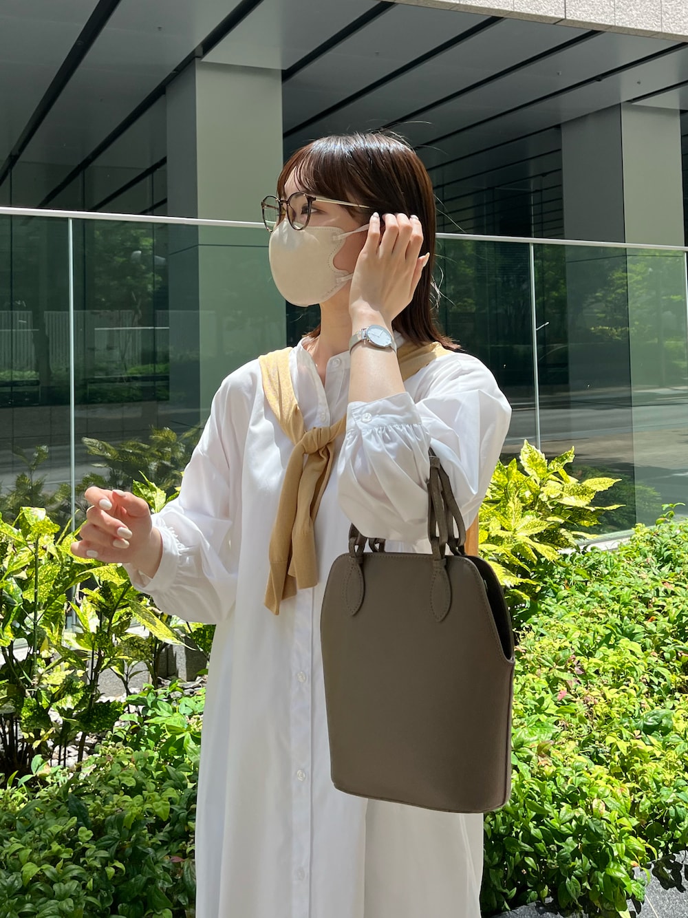 イエロー系のカーディガン/ボレロ、ホワイト系のシャツワンピース、ベージュ系のハンドバッグを着用したレディースの夏コーディネートの1枚目の写真