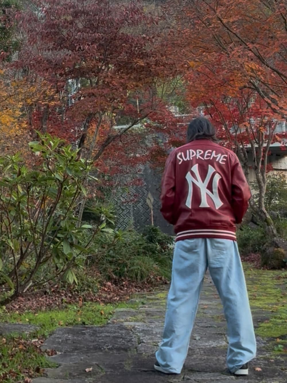 レッド系のスタジャン、ブルー系のデニムパンツ、ブラック系のスニーカーを着用したメンズの秋コーディネートの1枚目の写真