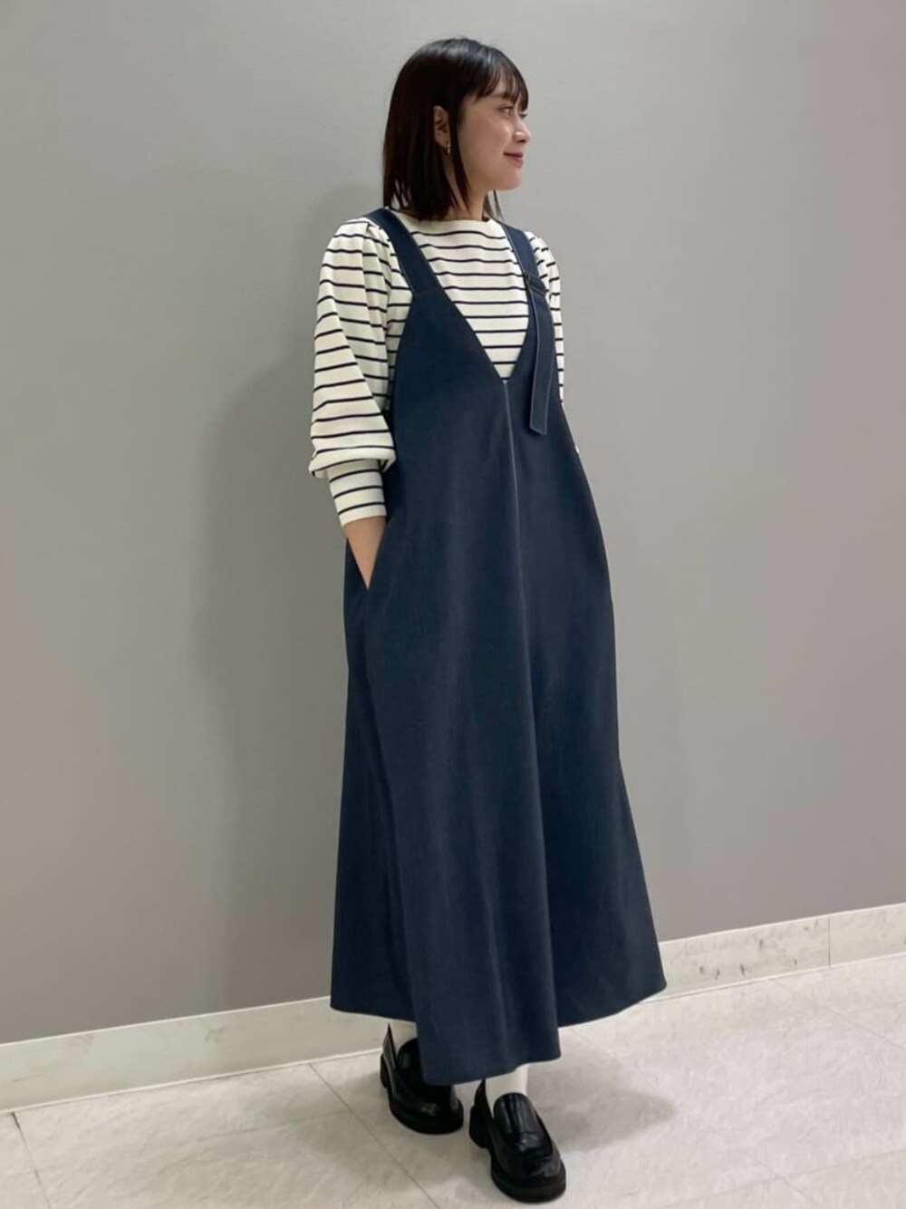 ホワイト系のニット/セーター、ブルー系のジャンパースカートを着用したレディースの冬コーディネートの1枚目の写真