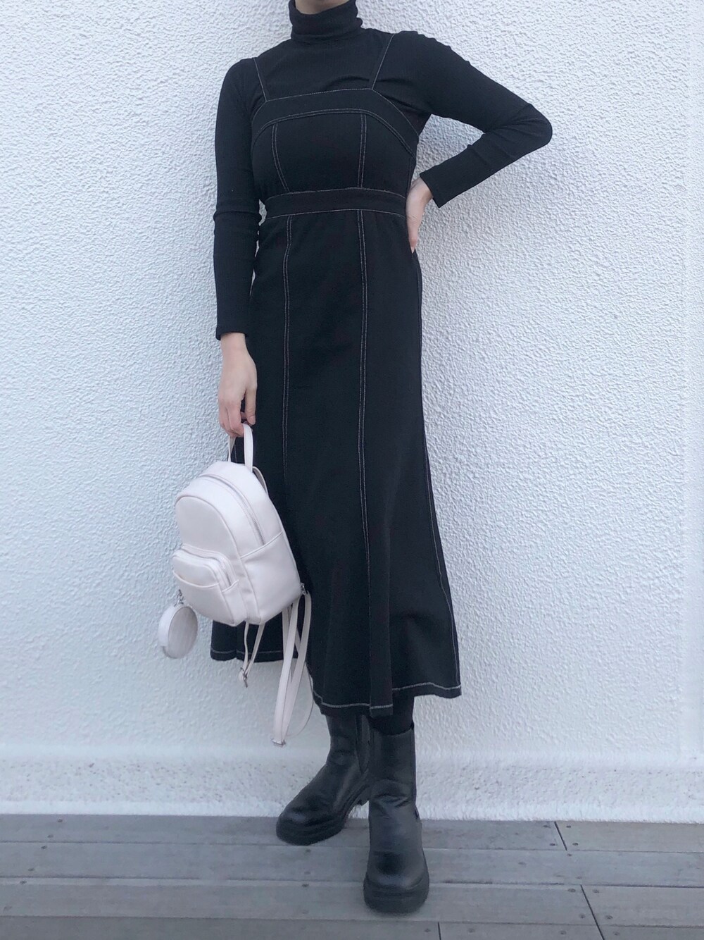 ブラック系のジャンパースカート、ブラック系のブーツ、ホワイト系のバックパック/リュックを着用したレディースの冬コーディネートの1枚目の写真