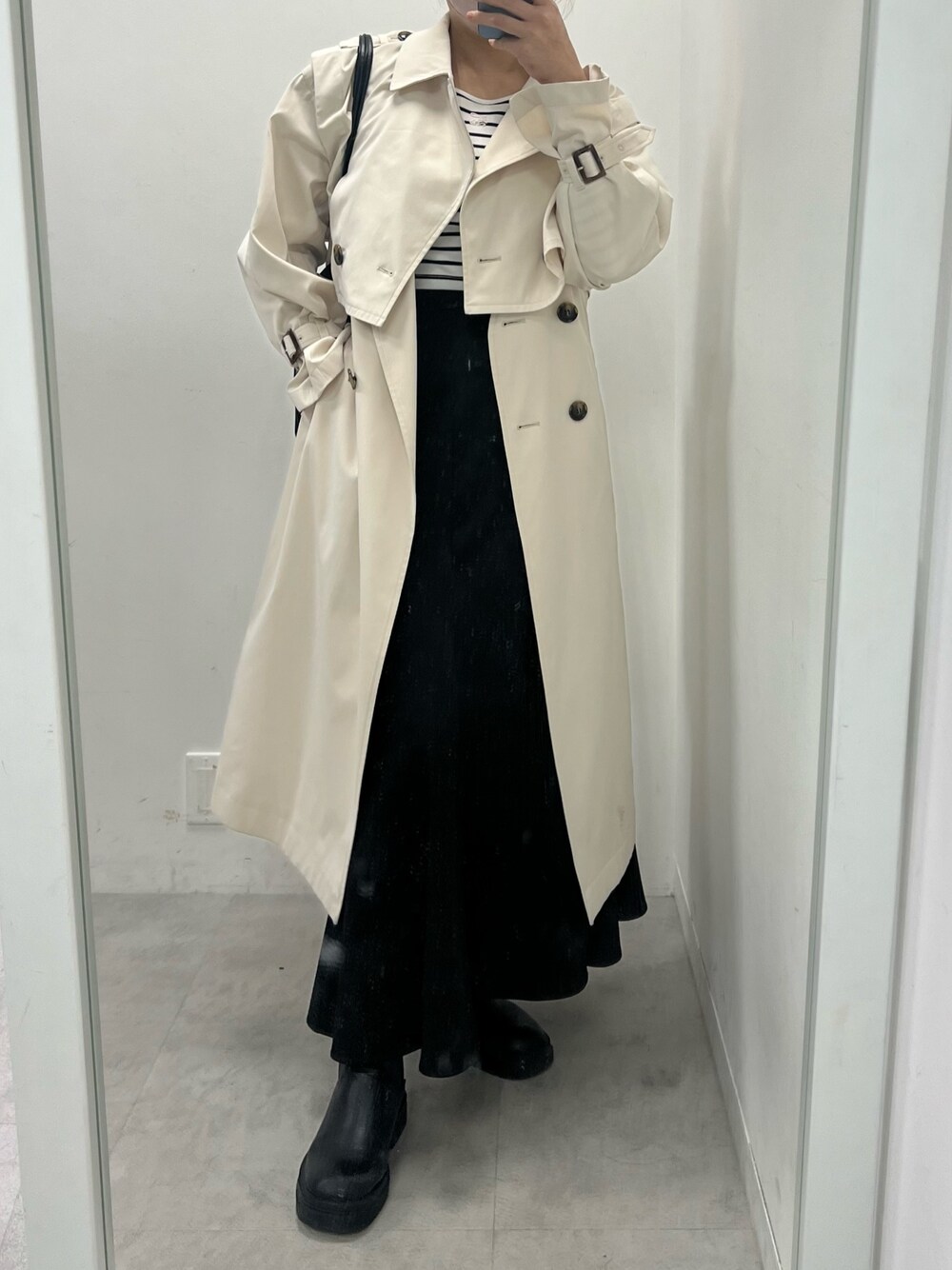ブラック系のスカート、ホワイト系のトレンチコート、ブラック系のブーツを着用したレディースの春コーディネートの1枚目の写真