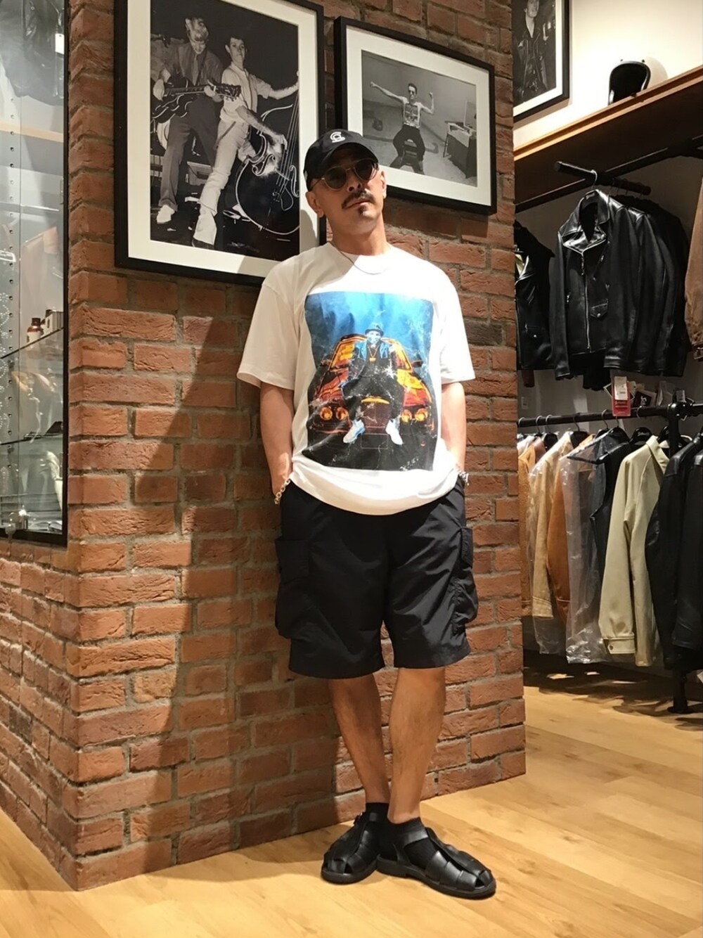 「メガネ男子、サンダル、キャップ、アメカジ、白Tシャツ、プリントT、ハーフパンツ、ショートパンツ、ビッグシルエット、ストリート」｜「WILD THINGSのSchottxWILDTHINGS/ショット×ワイルドシングス/CARGO SHORTS/カーゴショーツ（その他パンツ、ブラック系）」を使った、総料理長（schottのイケオジ）さん（メンズ・170cm）の夏コーディネートの1枚目の写真