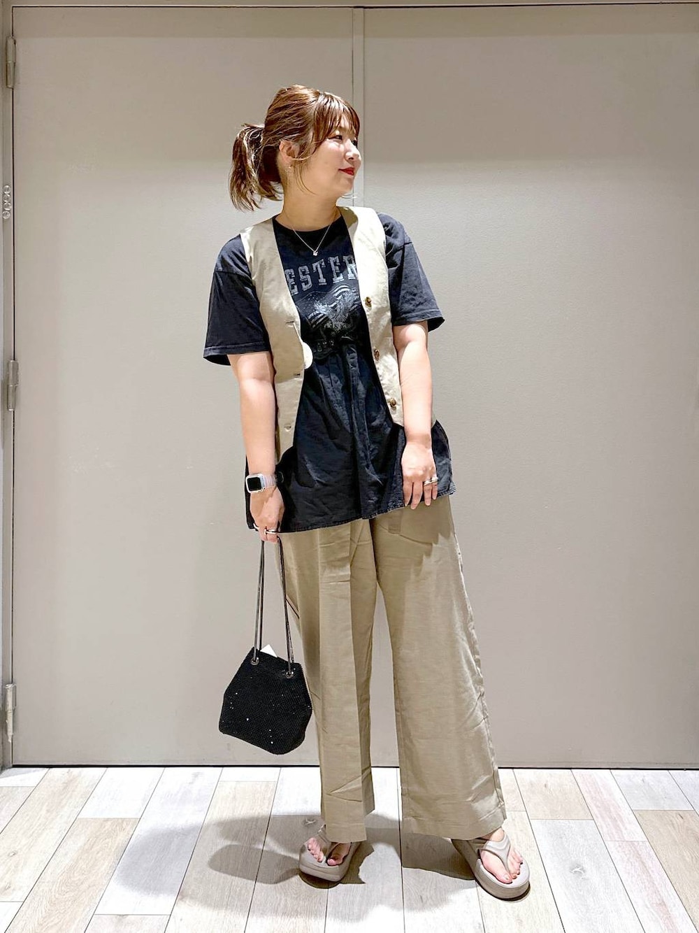 ブラック系のショルダーバッグ、ブラウン系のベスト、ベージュ系のサンダルを着用したレディースの夏コーディネートの1枚目の写真