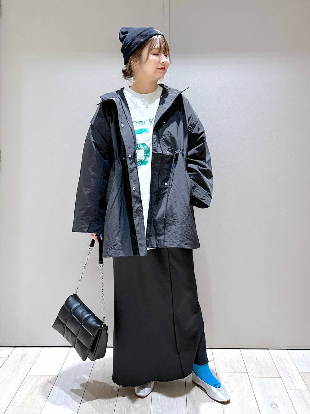 グレー系のチュニック、グレー系のパンプス、ブラック系のスカートを着用したレディースの春コーディネートの1枚目の写真