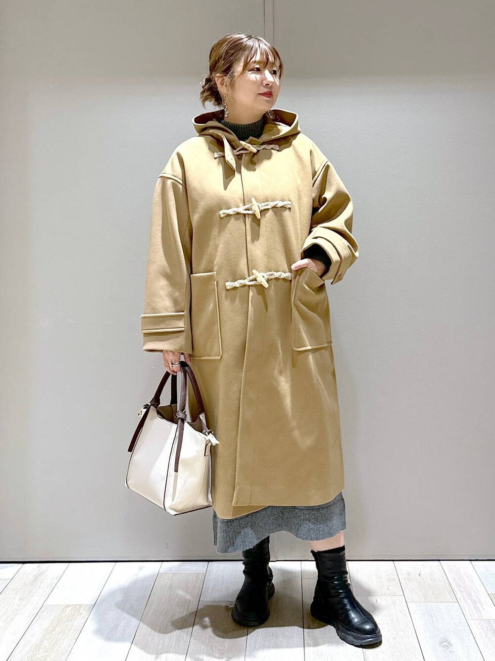 ベージュ系のショルダーバッグ、ブラウン系のダッフルコート、ブラック系のブーツを着用したレディースの冬コーディネートの1枚目の写真