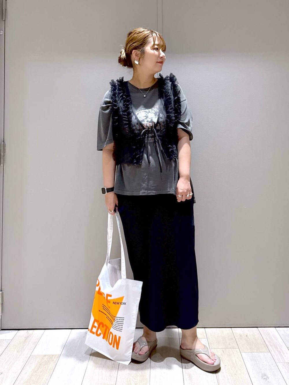 オレンジ系のトートバッグ、ブラック系のベスト、ベージュ系のサンダルを着用したレディースの夏コーディネートの1枚目の写真