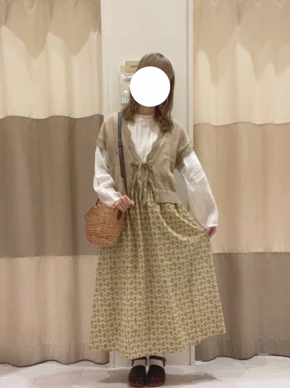 ベージュ系のベスト、ブラウン系のハンドバッグ、ベージュ系のスカートを着用したレディースの春コーディネートの1枚目の写真