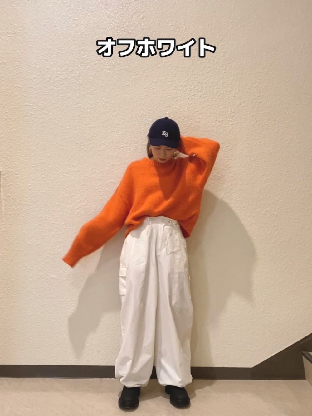 オレンジ系のニット/セーター、ホワイト系のカーゴパンツ、ブラック系のブーツを着用したレディースの冬コーディネートの1枚目の写真