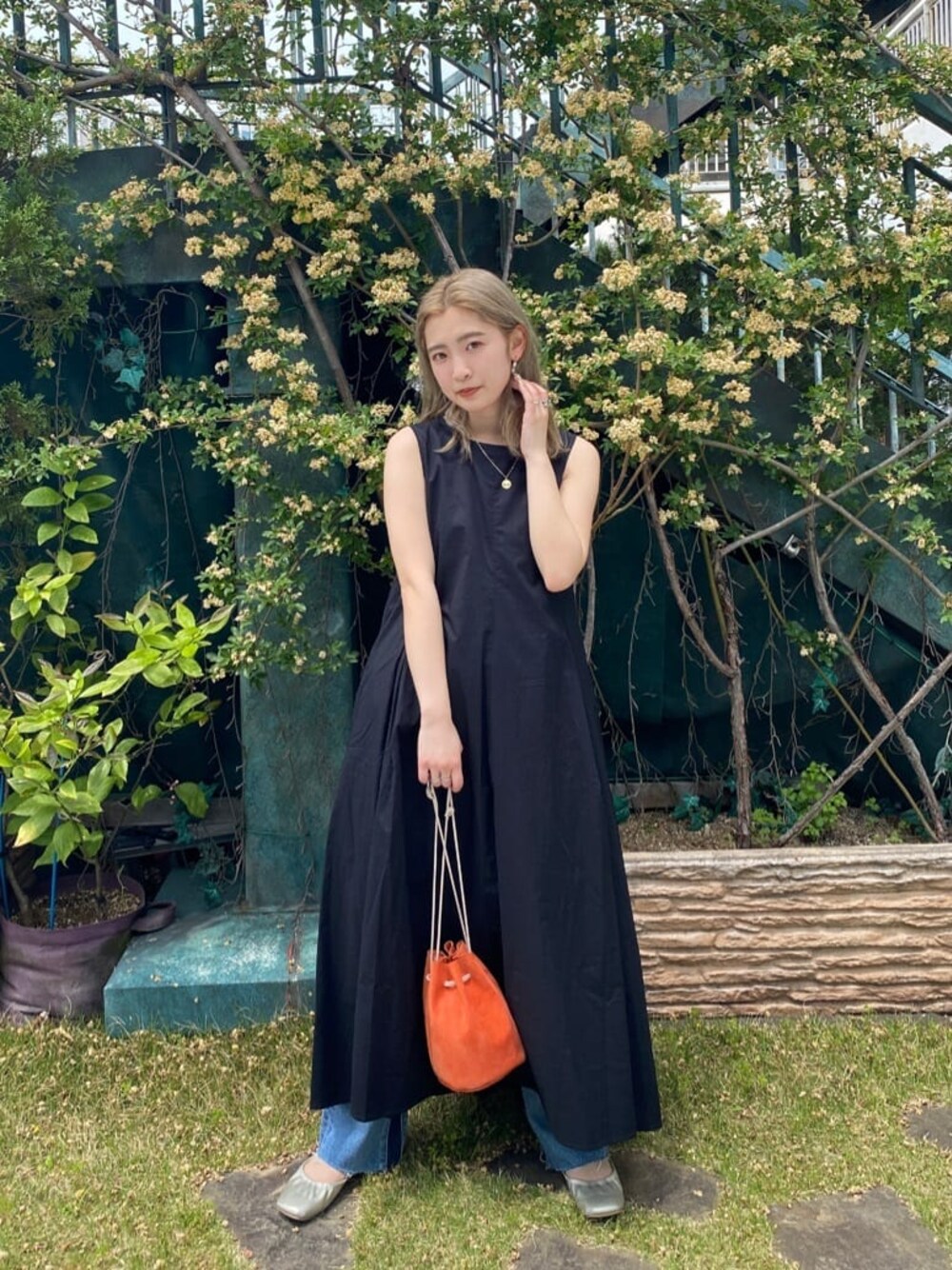 オレンジ系のハンドバッグ、ブルー系のデニムパンツ、ブラック系のワンピースを着用したレディースの春コーディネートの1枚目の写真