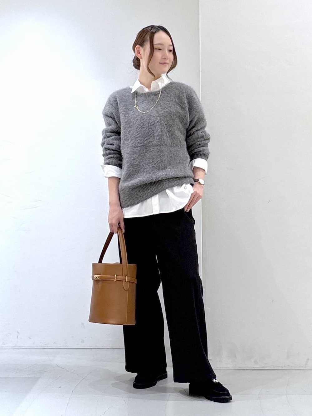 グレー系のニット/セーター、ホワイト系のシャツ/ブラウス、ブラック系のデニムパンツを着用したレディースの秋コーディネートの1枚目の写真