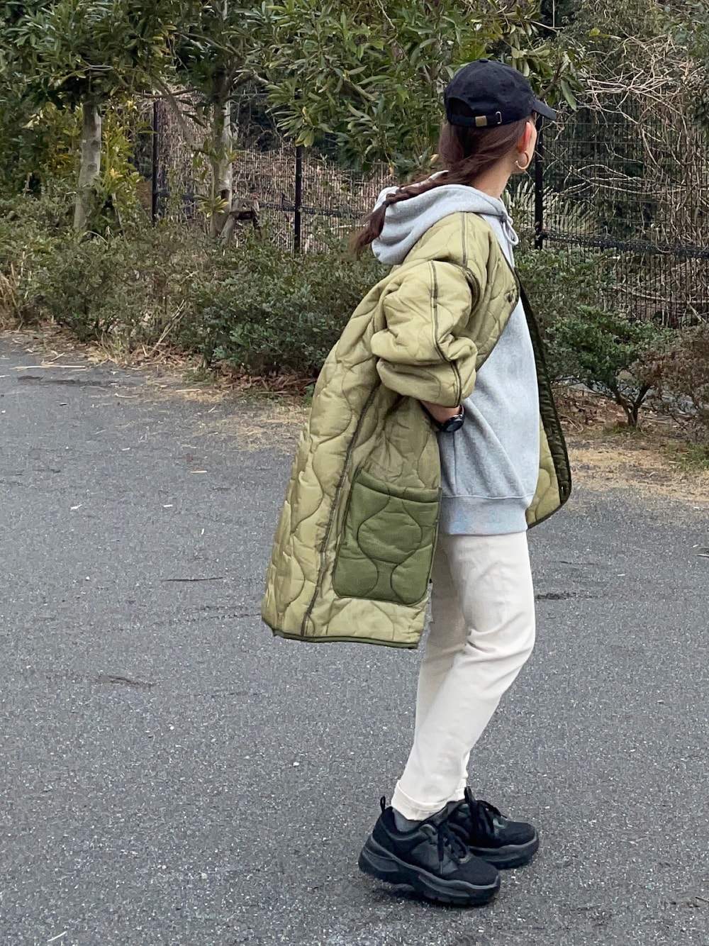 グレー系のパーカー、グリーン系のミリタリージャケット、ベージュ系のデニムパンツを着用したレディースの冬コーディネートの1枚目の写真