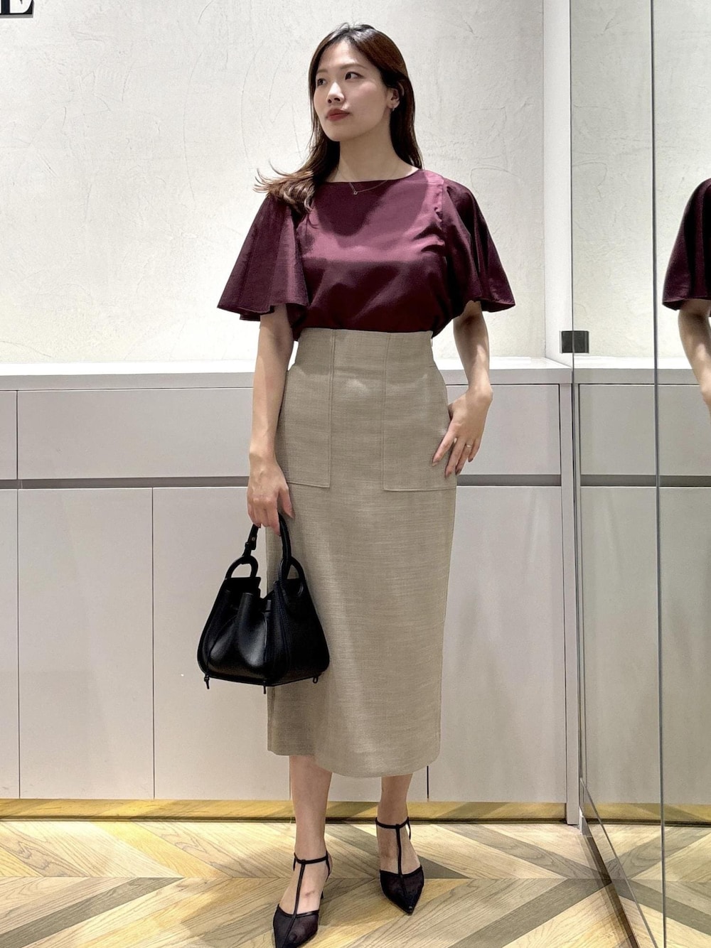 ブラック系のショルダーバッグ、ブラック系のパンプス、ベージュ系のスカートを着用したレディースの夏コーディネートの1枚目の写真