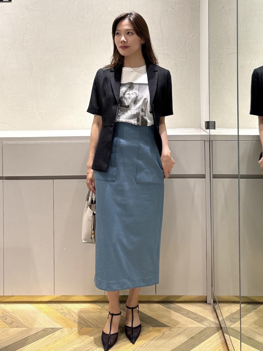 グレー系のハンドバッグ、ブラック系のパンプス、ブラック系のテーラードジャケットを着用したレディースの夏コーディネートの1枚目の写真