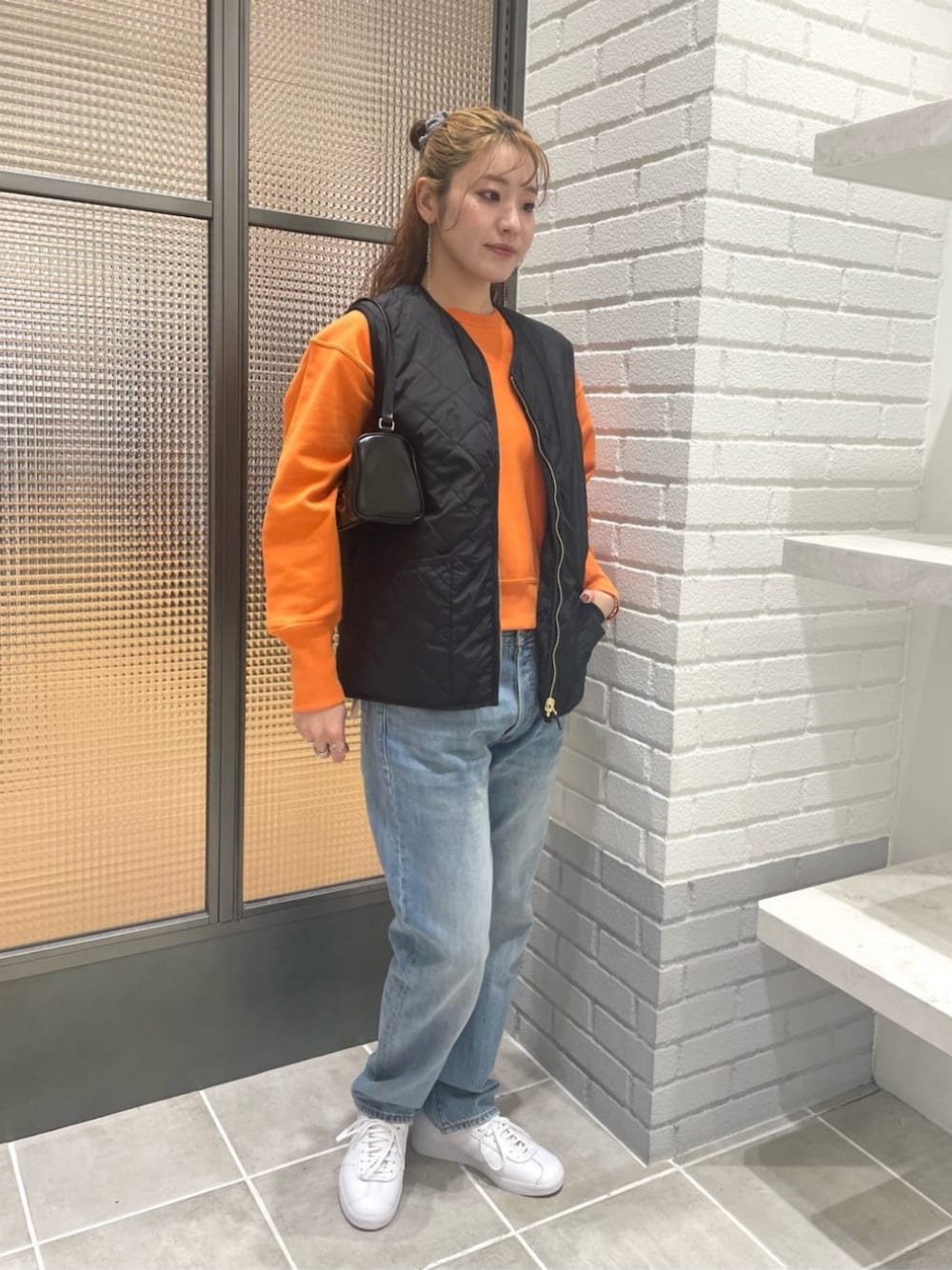 ブラック系のベスト、オレンジ系のスウェット、ブルー系のデニムパンツを着用したレディースの秋コーディネートの1枚目の写真