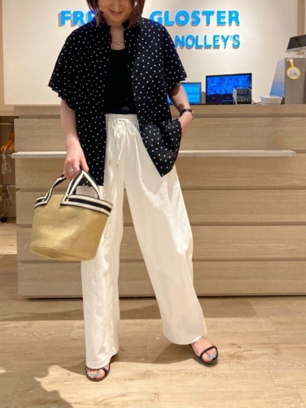 ブラック系のシャツ/ブラウス、ホワイト系のスラックス、ベージュ系のトートバッグを着用したレディースの春コーディネートの1枚目の写真