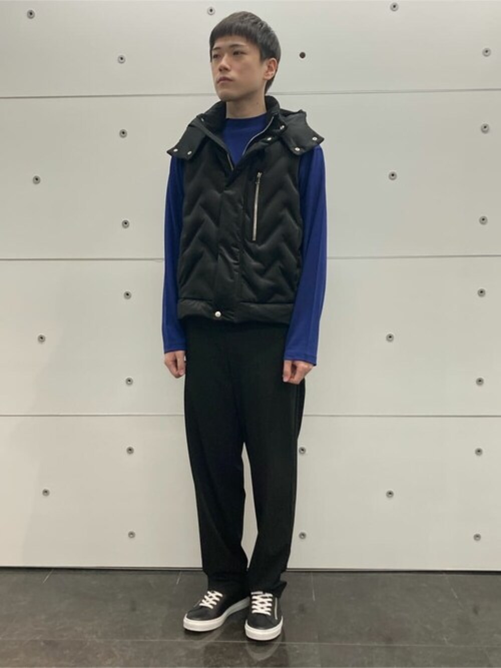 ブラック系のダウンベスト、ブルー系のTシャツ/カットソー、ブラック系のスラックスを着用したメンズの冬コーディネートの1枚目の写真