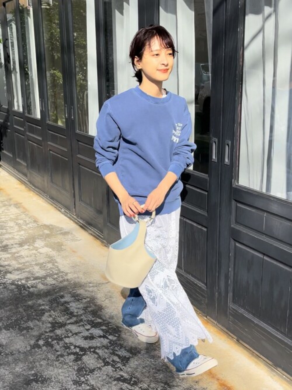 ブルー系のデニムパンツ、ブルー系のスウェット、ホワイト系のハンドバッグを着用したレディースの冬コーディネートの1枚目の写真