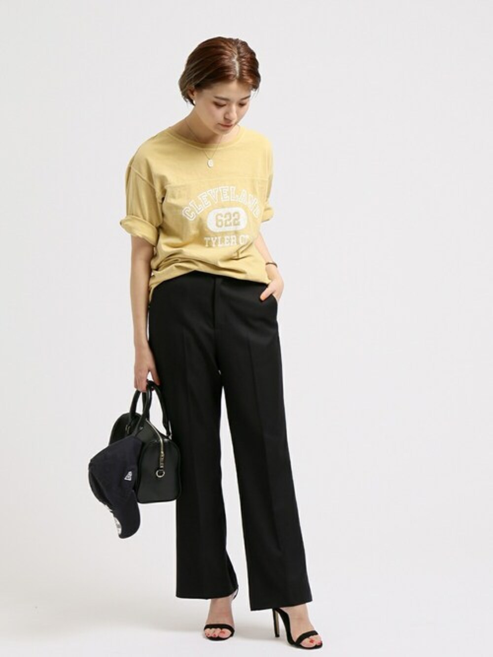 ブラック系のスラックス、ブラック系のボストンバッグ、イエロー系のTシャツ/カットソーを着用したレディースの春コーディネートの1枚目の写真