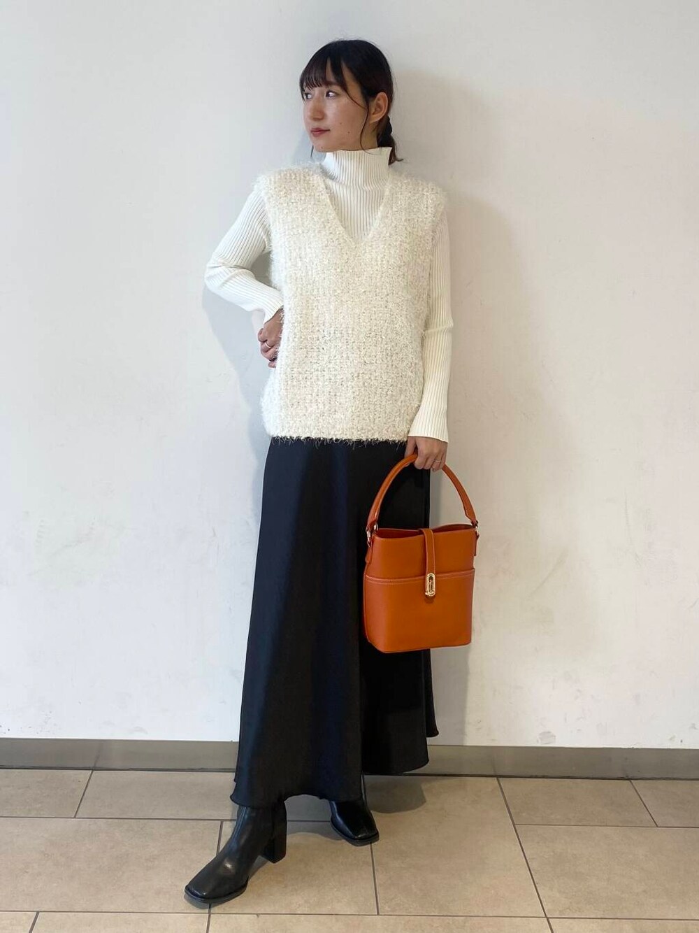 ホワイト系のニット/セーター、オレンジ系のハンドバッグ、ブラック系のブーツを着用したレディースの秋コーディネートの1枚目の写真