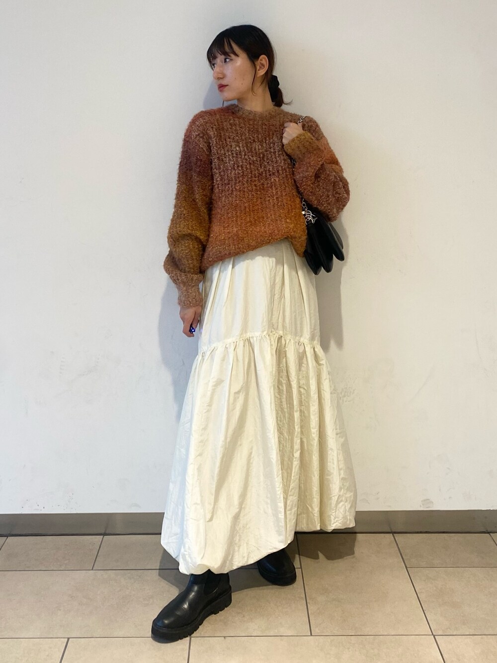 ホワイト系のスカート、オレンジ系のニット/セーター、ブラック系のブーツを着用したレディースの秋コーディネートの1枚目の写真