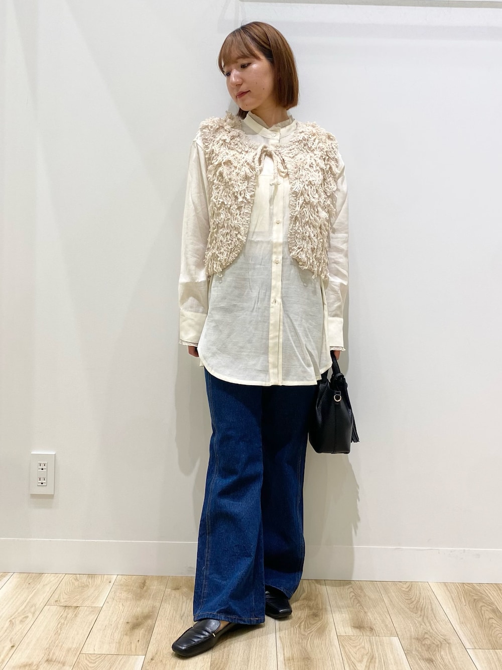 ベージュ系のベスト、ブルー系のデニムパンツ、ブラック系のショルダーバッグを着用したレディースの秋コーディネートの1枚目の写真