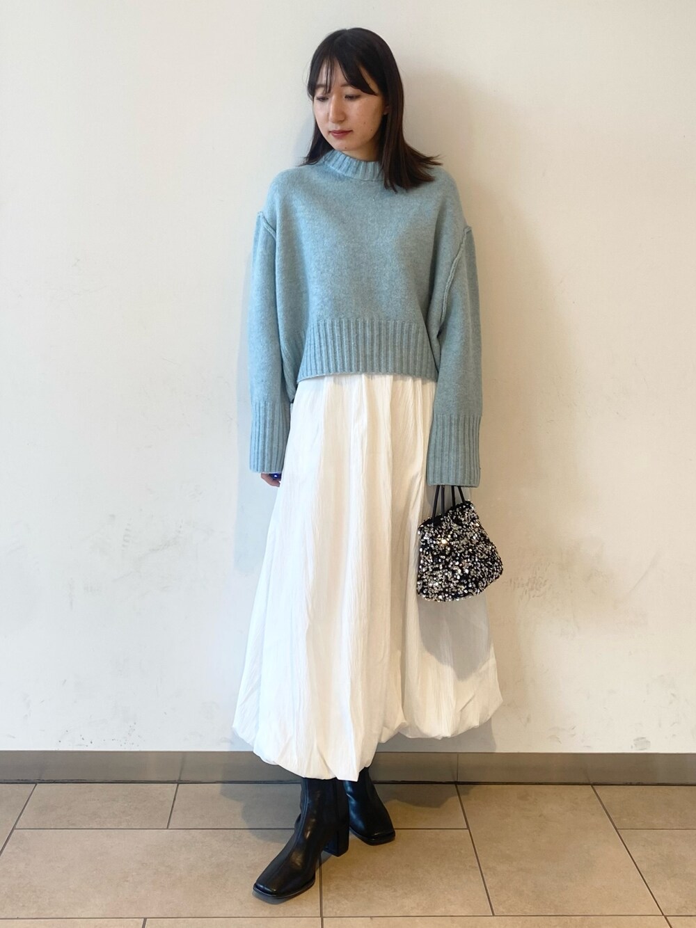 ホワイト系のスカート、ブルー系のニット/セーター、ブラック系のブーツを着用したレディースの冬コーディネートの1枚目の写真