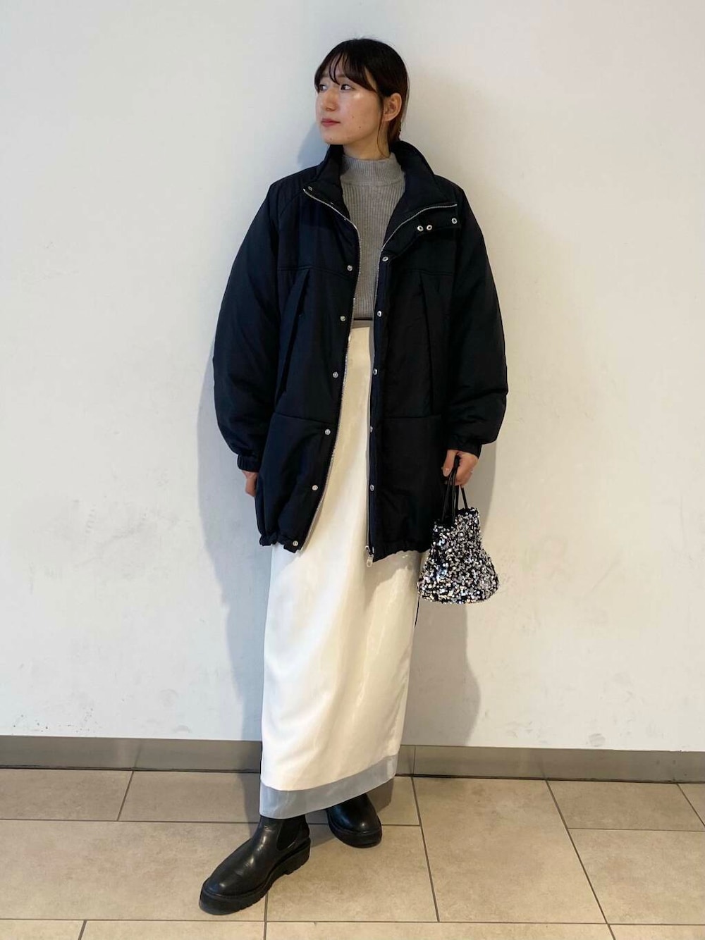 ブラック系のブーツ、グレー系のニット/セーター、ホワイト系のスカートを着用したレディースの冬コーディネートの1枚目の写真