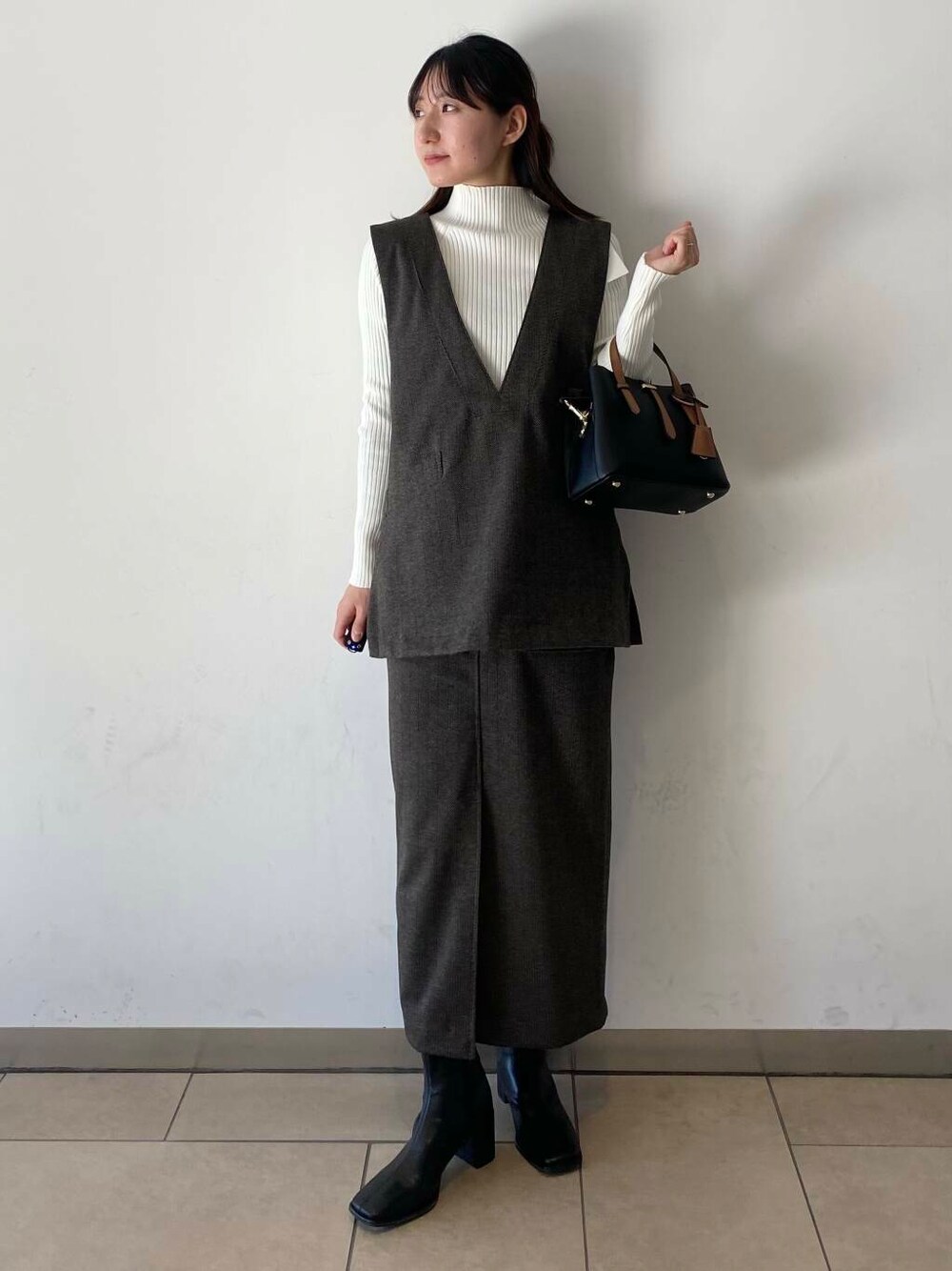 ブラック系のハンドバッグ、ホワイト系のニット/セーター、ブラック系のブーツを着用したレディースの冬コーディネートの1枚目の写真