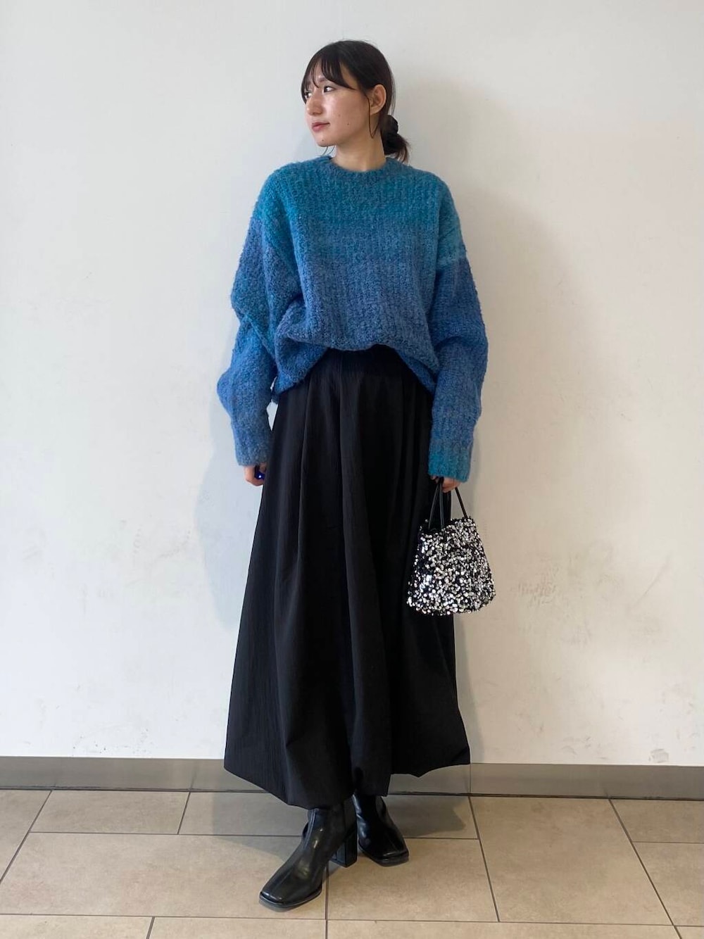 ブラック系のスカート、シルバー系のショルダーバッグ、ブラック系のブーツを着用したレディースの冬コーディネートの1枚目の写真