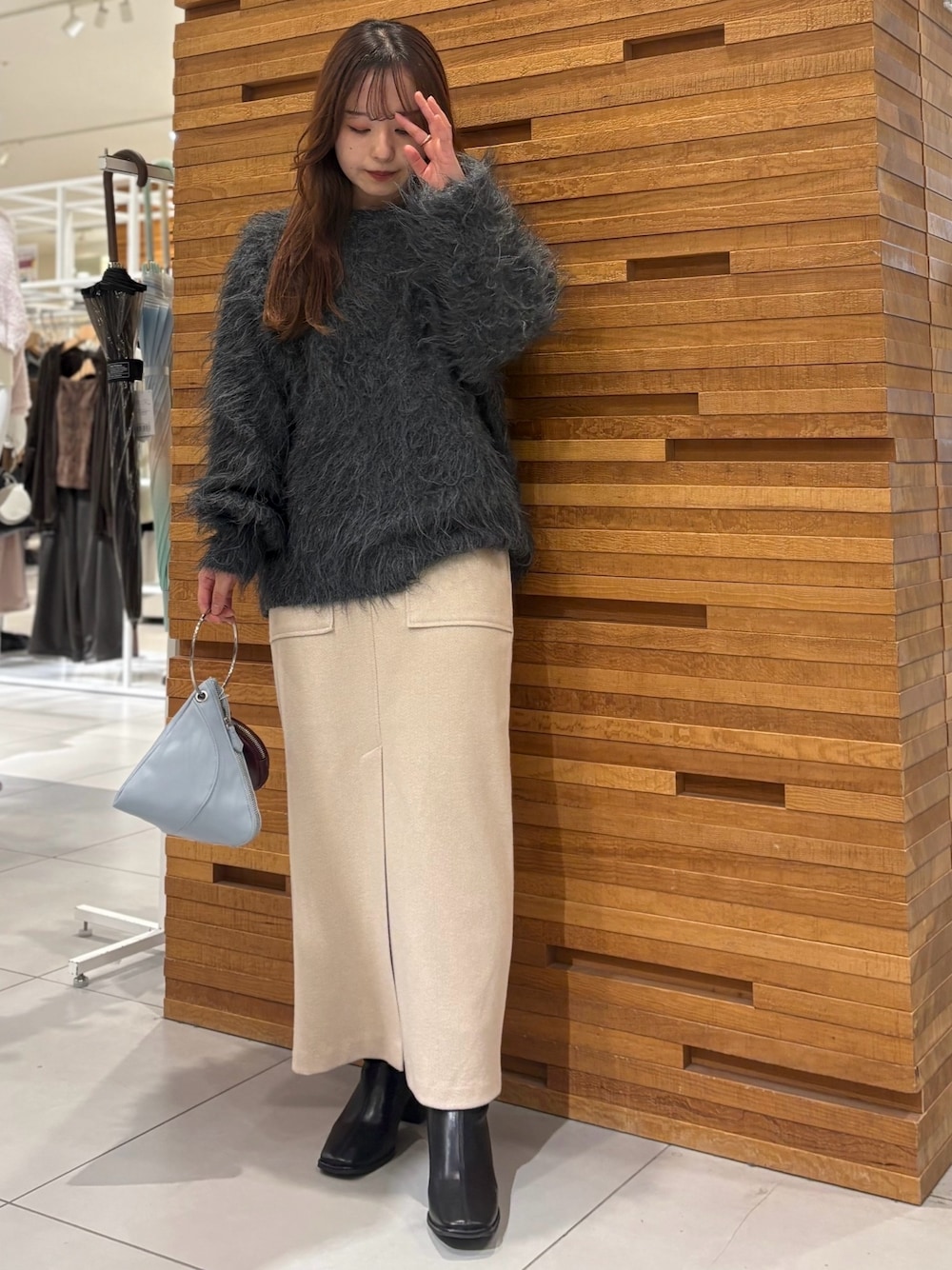 グレー系のニット/セーター、ブラウン系のスカート、ブルー系のハンドバッグを着用したレディースの秋コーディネートの1枚目の写真