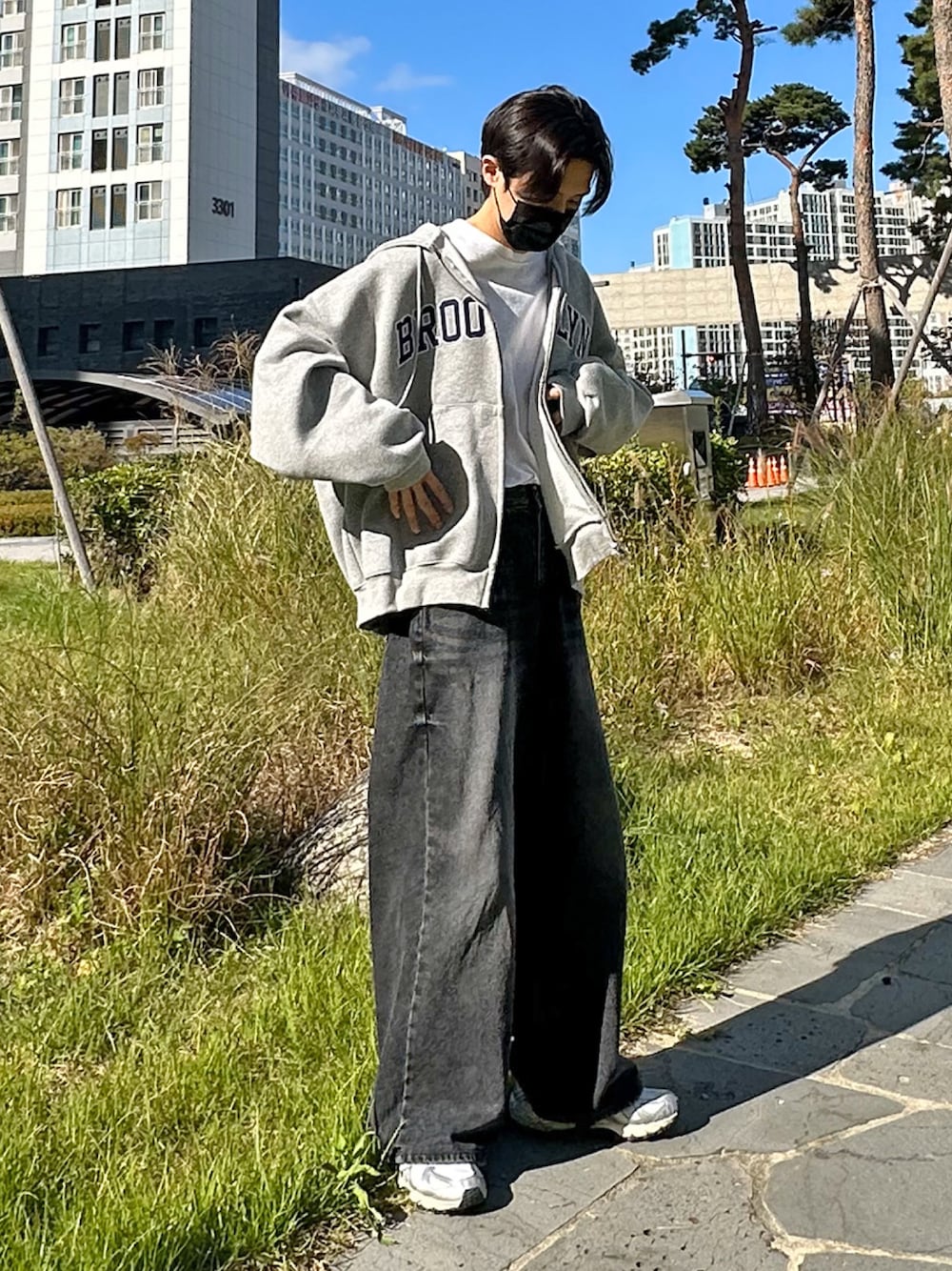 グレー系のパーカー、シルバー系のスニーカー、ブラック系のデニムパンツを着用したメンズの秋コーディネートの1枚目の写真