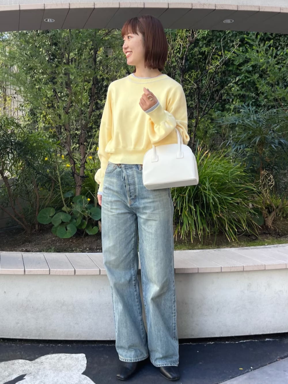 イエロー系のニット/セーター、ホワイト系のボストンバッグ、ブルー系のデニムパンツを着用したレディースの冬コーディネートの1枚目の写真