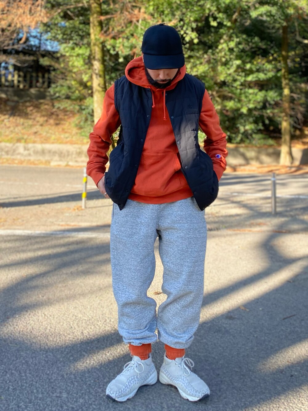 オレンジ系のパーカー、ブラック系のノーカラージャケット、グレー系のスウェットパンツを着用したメンズの冬コーディネートの1枚目の写真
