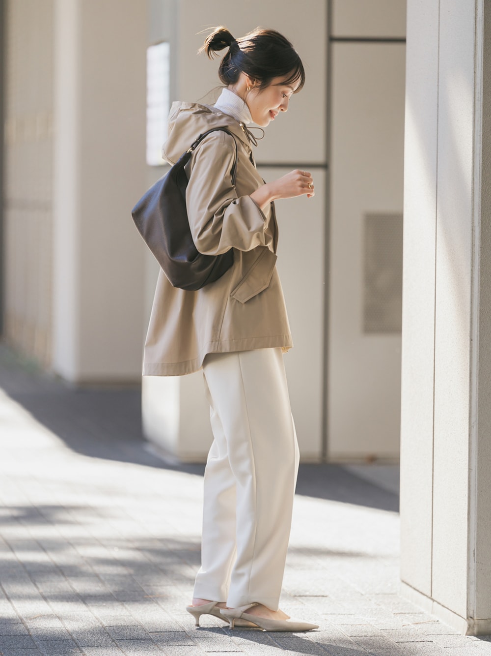 ベージュ系のマウンテンパーカー、ブラウン系のショルダーバッグ、ホワイト系のスラックスを着用したレディースの冬コーディネートの1枚目の写真