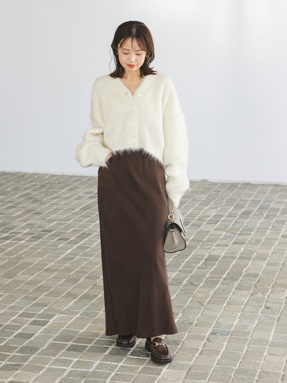 ホワイト系のカーディガン/ボレロ、ブラウン系のスカート、グレー系のショルダーバッグを着用したレディースの秋コーディネートの1枚目の写真