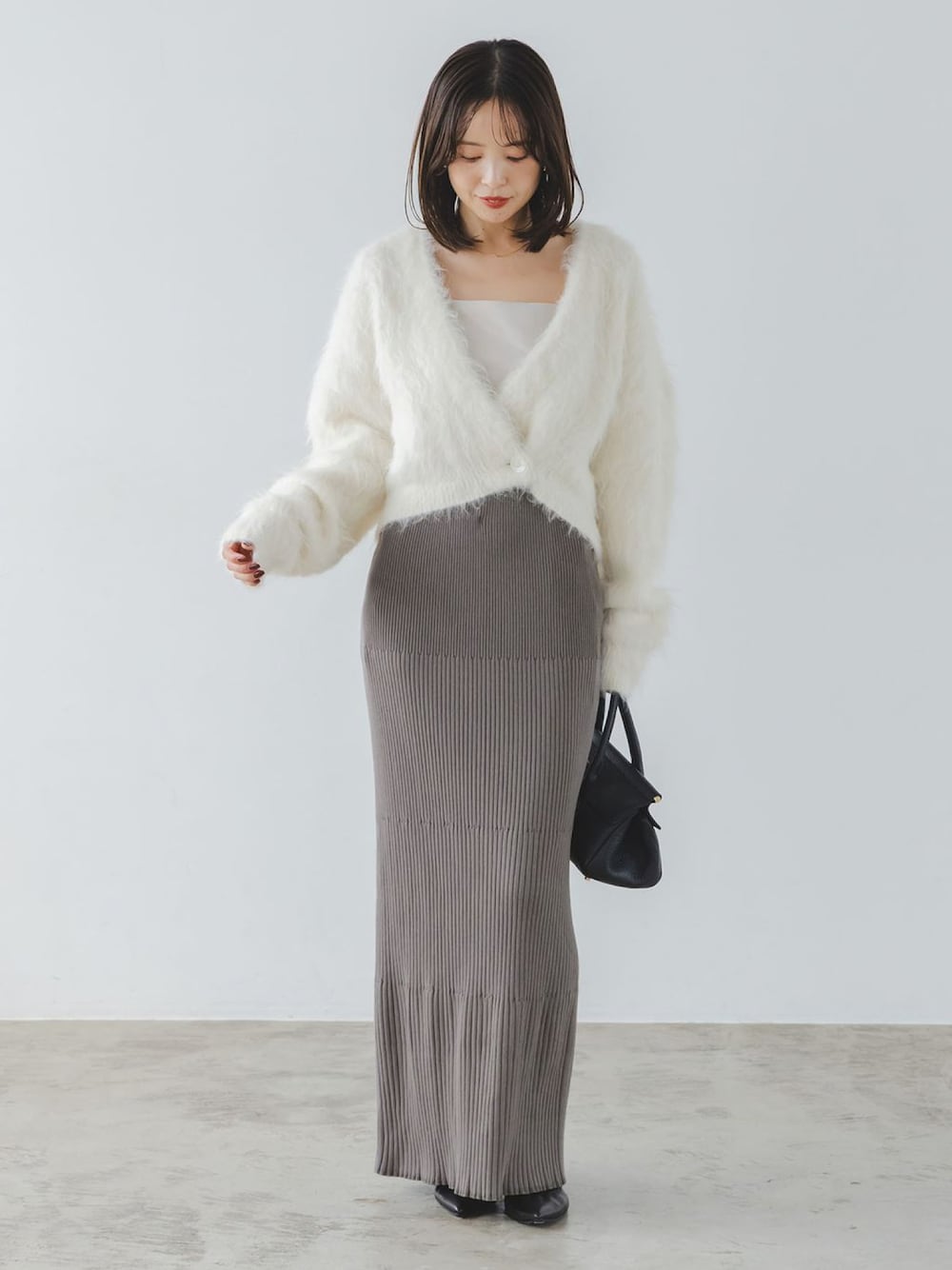 ホワイト系のカーディガン/ボレロ、グレー系のスカート、イエロー系のボストンバッグを着用したレディースの秋コーディネートの1枚目の写真