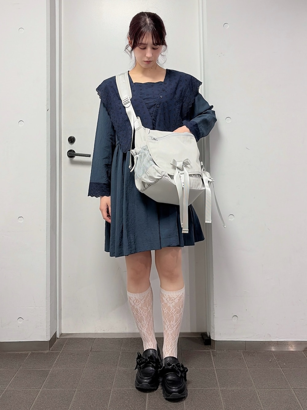 ブルー系のワンピース、ベージュ系のメッセンジャーバッグ、ブラック系のスニーカーを着用したレディースの冬コーディネートの1枚目の写真