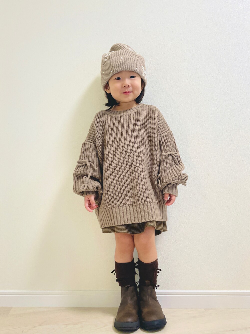 ベージュ系のニット/セーター、ブラウン系のブーツ、ベージュ系のニットキャップ/ビーニーを着用したキッズの秋コーディネートの1枚目の写真