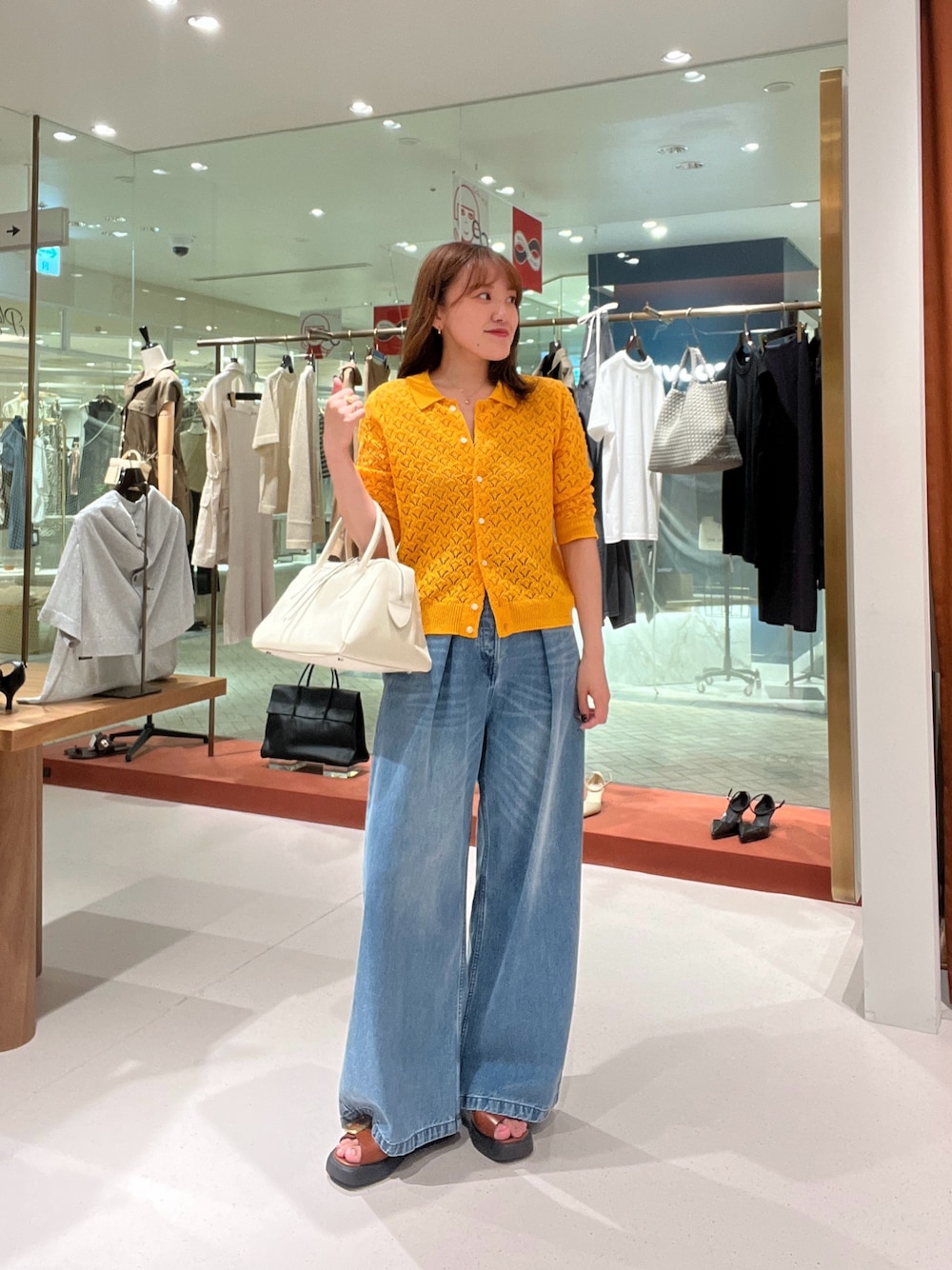 オレンジ系のニット/セーター、ホワイト系のトートバッグ、ブルー系のデニムパンツを着用したレディースの夏コーディネートの1枚目の写真