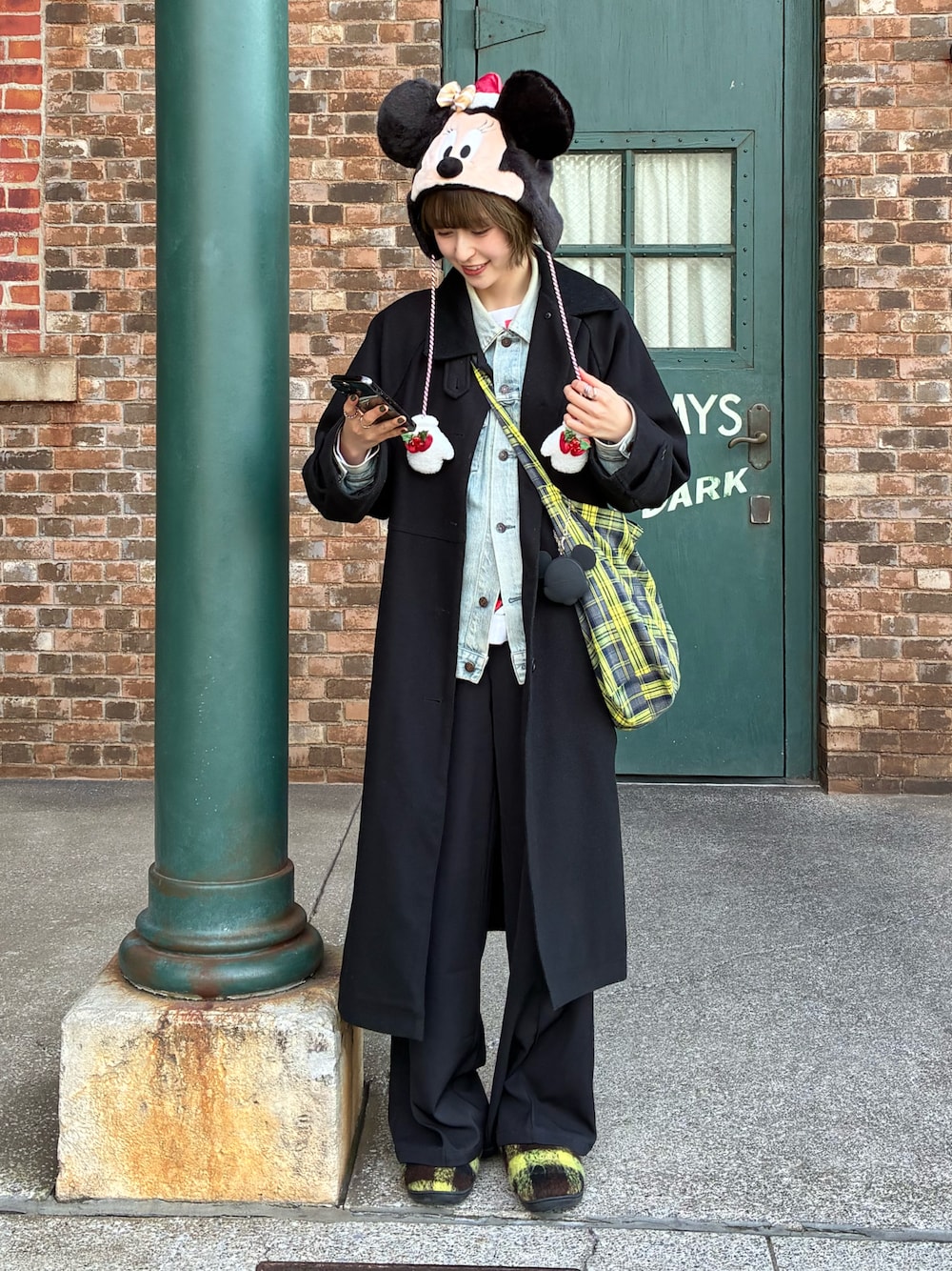 イエロー系のショルダーバッグ、ブラック系のステンカラーコート、イエロー系のスリッポンを着用したレディースの冬コーディネートの1枚目の写真