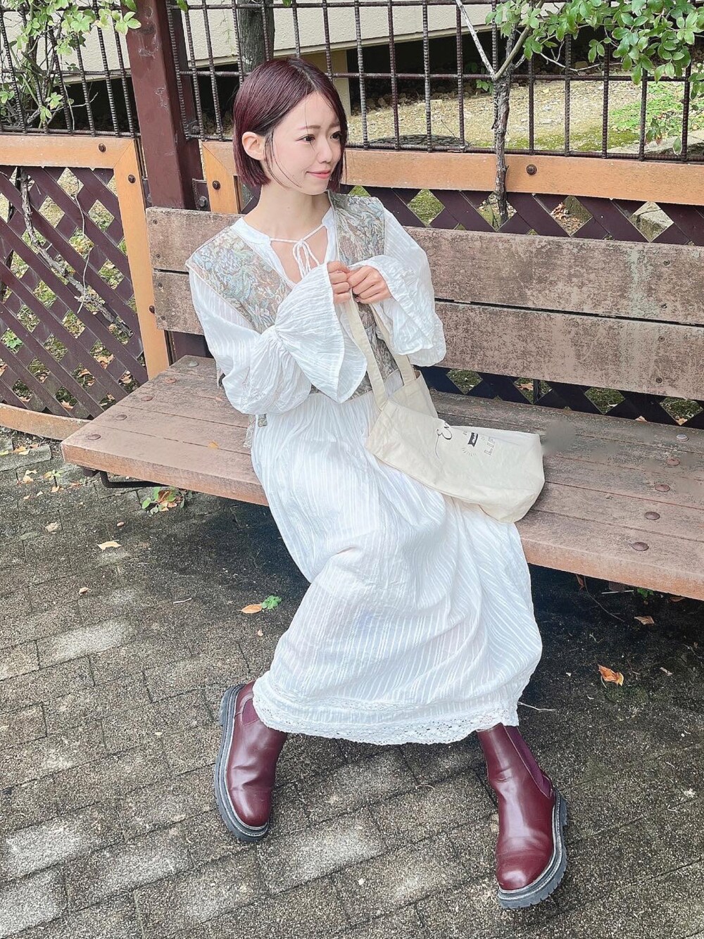 レッド系のブーツ、グリーン系のベスト、ホワイト系のワンピースを着用したレディースの冬コーディネートの1枚目の写真