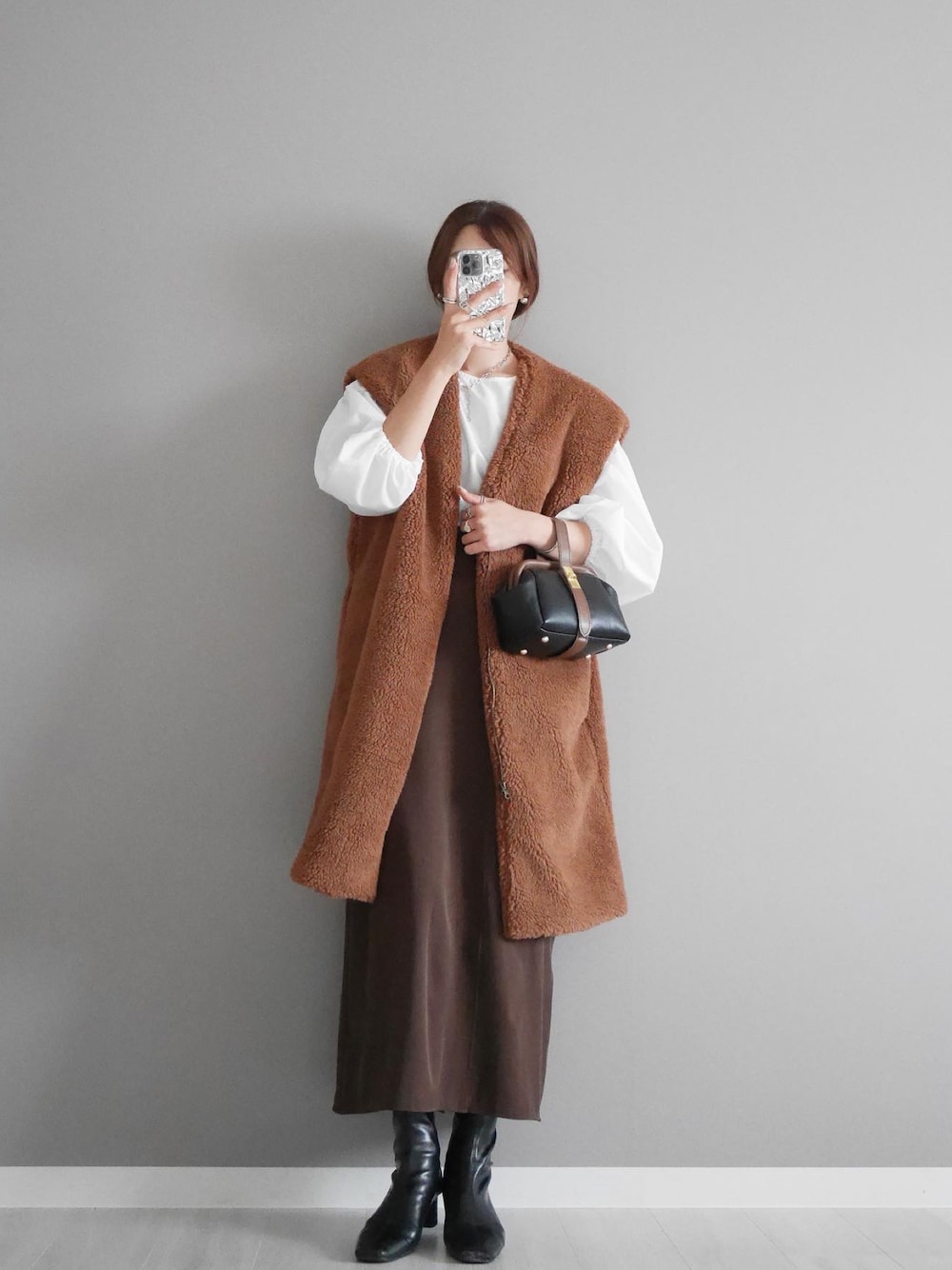 ブラウン系のベスト、ブラウン系のスカート、ブラック系のショルダーバッグを着用したレディースの秋コーディネートの1枚目の写真