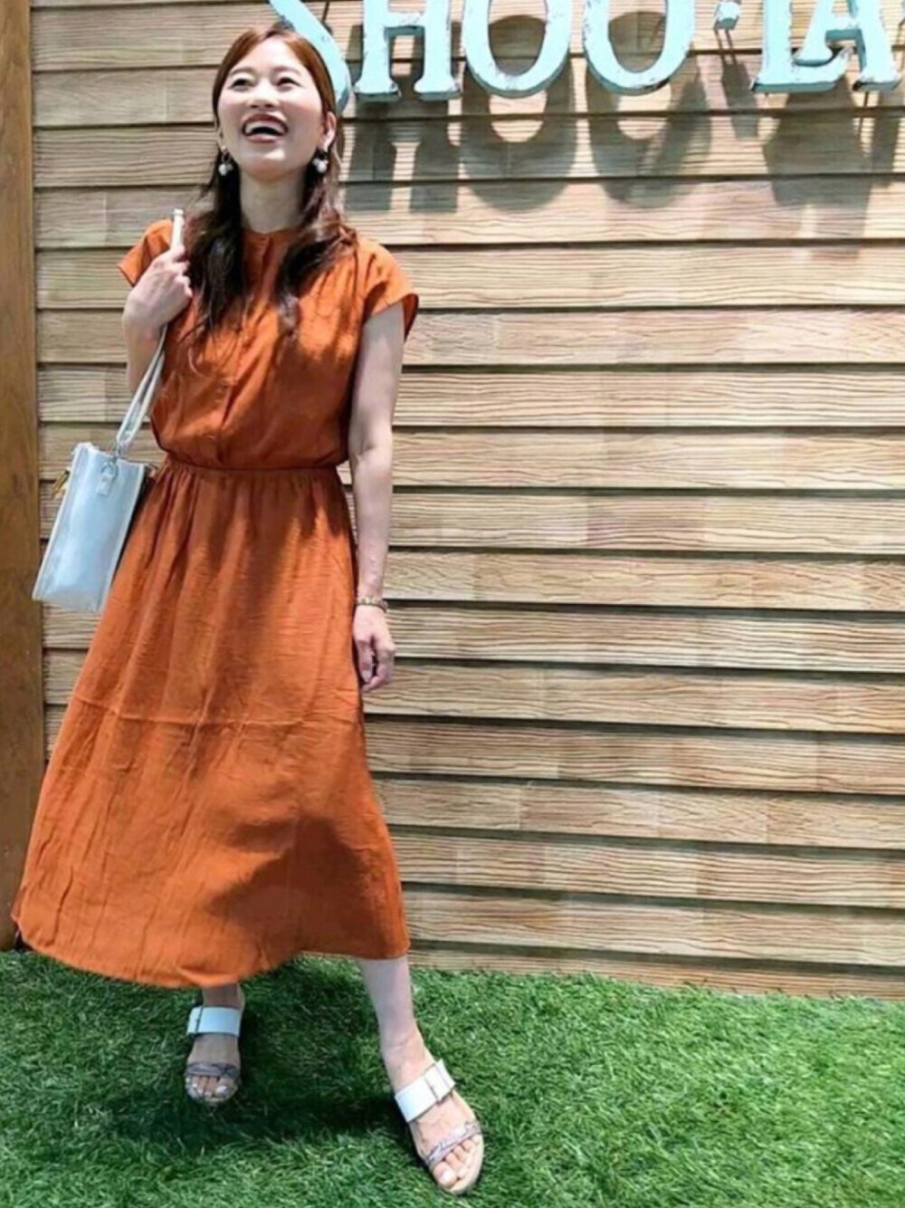 オレンジ系のワンピース、ホワイト系のトートバッグ、ベージュ系のサンダルを着用したレディースの秋コーディネートの1枚目の写真